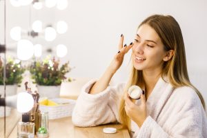 young-girl-cares-face-skin-with-moisturizer-front-of-mirror